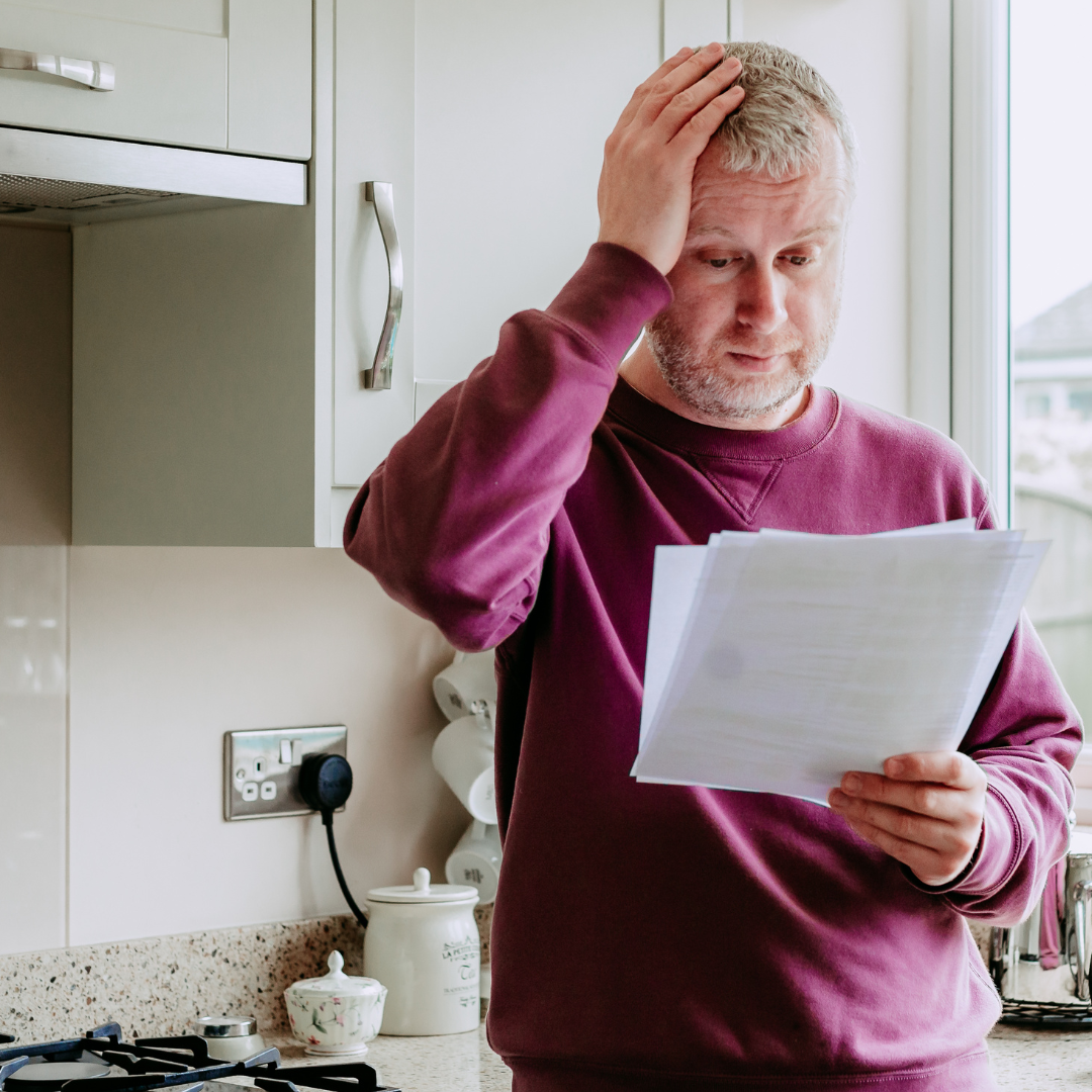 Man in maroon jumper holding a piece of paper and his head